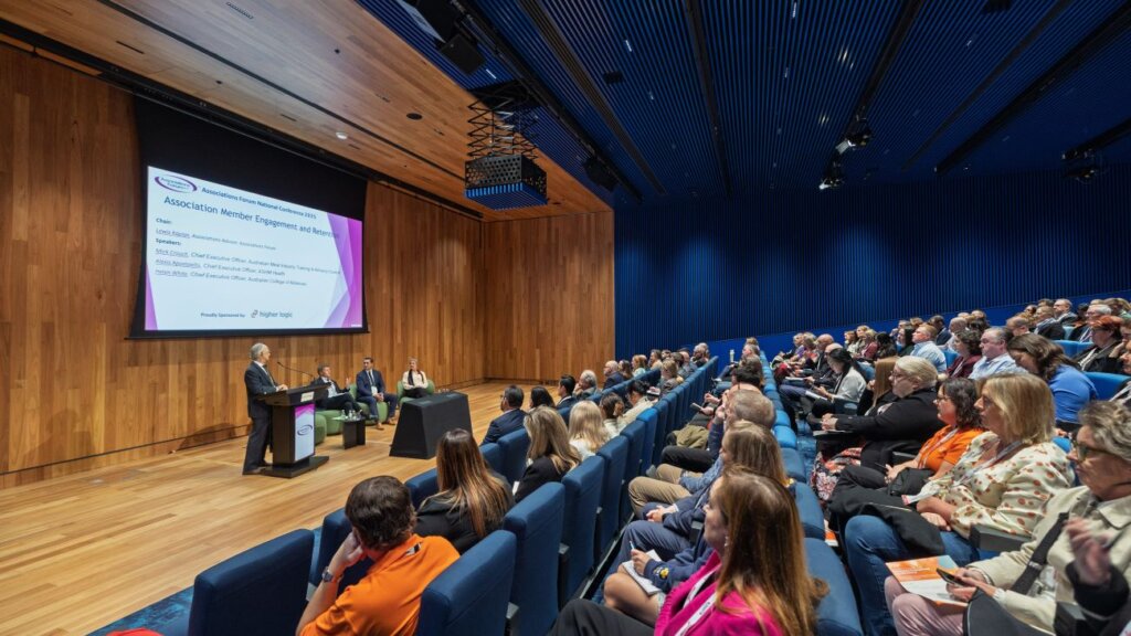 A large audience seated in a lecture hall during the Associations Forum National Conference, with a presentation screen visible.