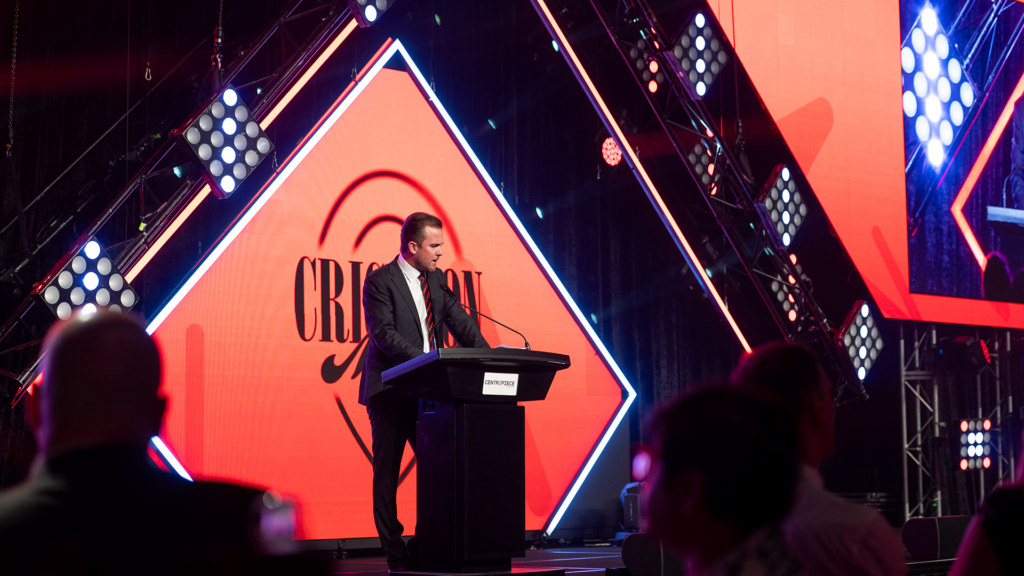 A man presenting to an audience at a banquet event.